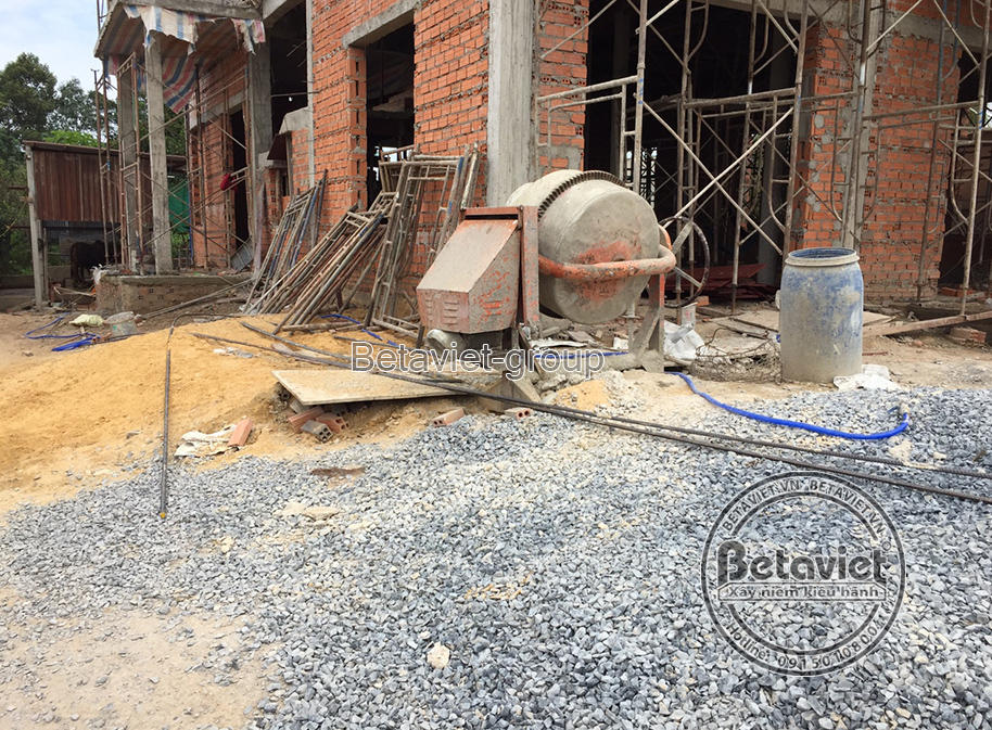 Khu vực tập kết vật liệu và máy móc phục vụ thi công phần thô, nhìn từ góc thấp. Máy trộn bê tông đang hoạt động, cùng với…