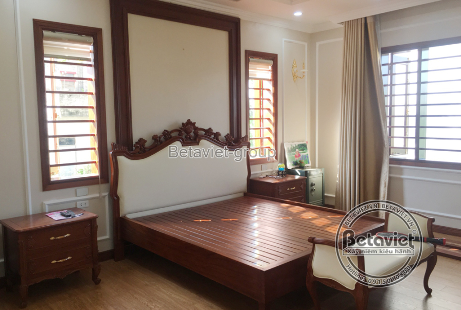 Phòng ngủ master với giường gỗ lớn, đầu giường bọc nệm trắng tinh tế, kết hợp tủ đầu giường gỗ nhỏ gọn. Tường màu kem tran…
