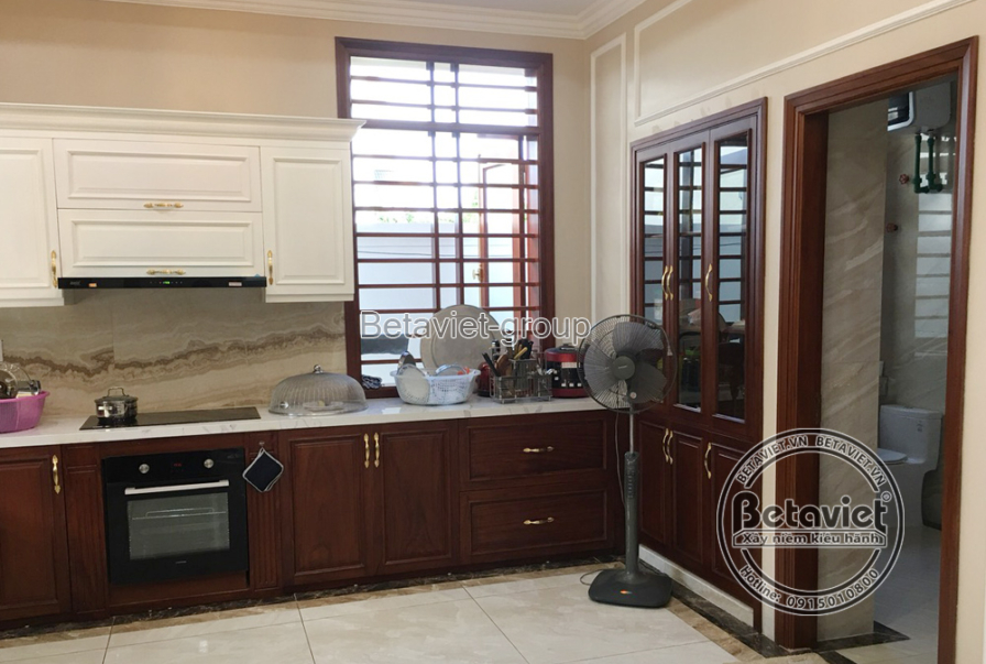 Khu vực bếp gọn gàng với tủ bếp trên màu trắng kem và tủ bếp dưới màu nâu gỗ, mặt bếp ốp đá vân mây. Thiết bị bếp hiện đại…