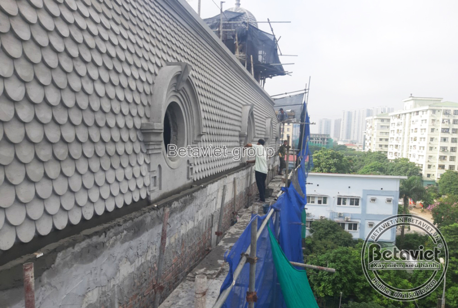 Toàn cảnh mái vòm ngói vảy cá nhìn dọc theo giàn giáo từ trên cao, phía xa là các tòa chung cư cao tầng của Hà Nội. Từng p…
