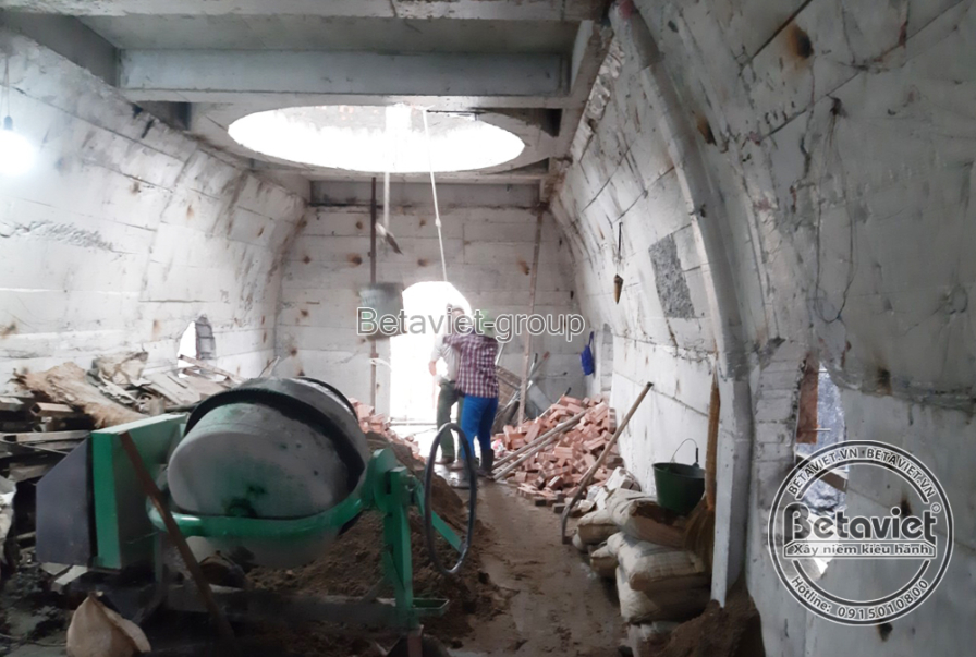 Căn phòng cong với giếng trời hình oval phía trên, máy trộn bê tông đặt giữa phòng, tường bê tông còn thô ráp. Một công nh…
