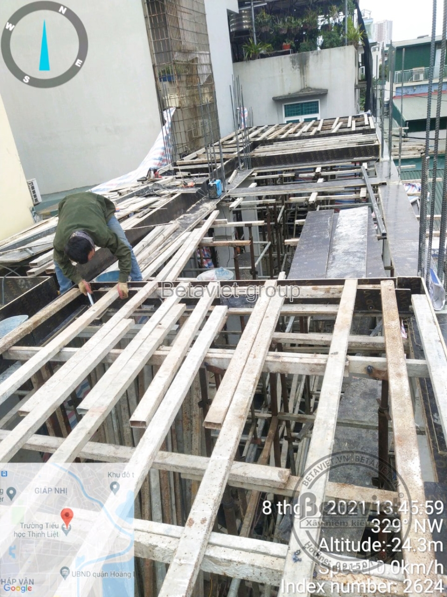 Cận cảnh lưới thép sàn đặt trên ván khuôn gỗ với hệ đà đỡ bên dưới, một công nhân cúi người kiểm tra và buộc mối nối thép…