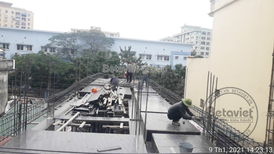 Toàn cảnh sàn bê tông cốt thép rộng đang thi công với rãnh ván khuôn dầm, một công nhân cúi làm việc ở góc xa. Phía sau là…