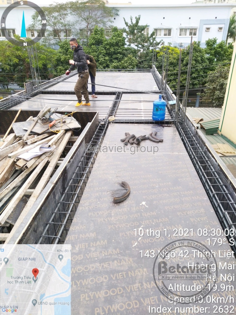 Sàn thép chờ đổ bê tông với ván khuôn viền gỗ, bìa carton và vật liệu thừa rải rác trên bề mặt. Một công nhân bước ngang s…