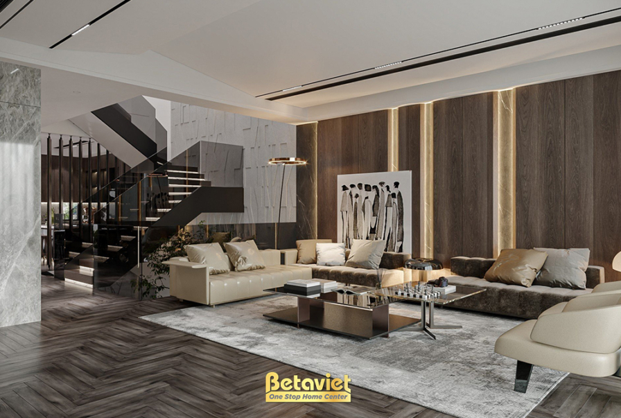 Phòng khách nhìn thấy cầu thang phía sau, tường đá ốp cùng tranh treo, cụm sofa và thảm lông dày, ánh đèn vàng ấm tạo chiề…