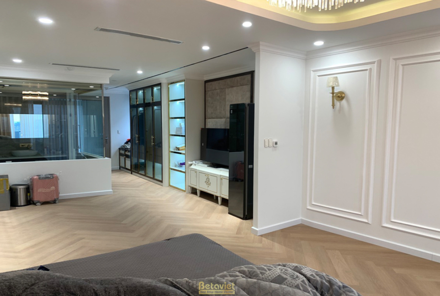Không gian phòng khách sang trọng với sofa da màu nâu, bàn trà đá. Tường ốp phào chỉ trắng, sàn gỗ xương cá. Ánh sáng vàng…