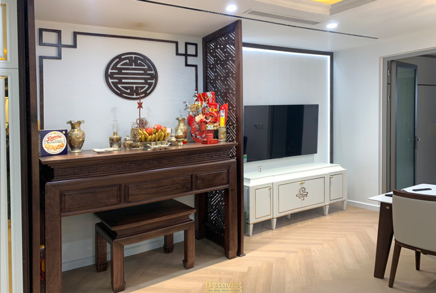Không gian phòng khách hoặc sinh hoạt chung với tủ gỗ chạm khắc, kệ tivi màu trắng. Sàn gỗ xương cá, vách ngăn gỗ trang tr…