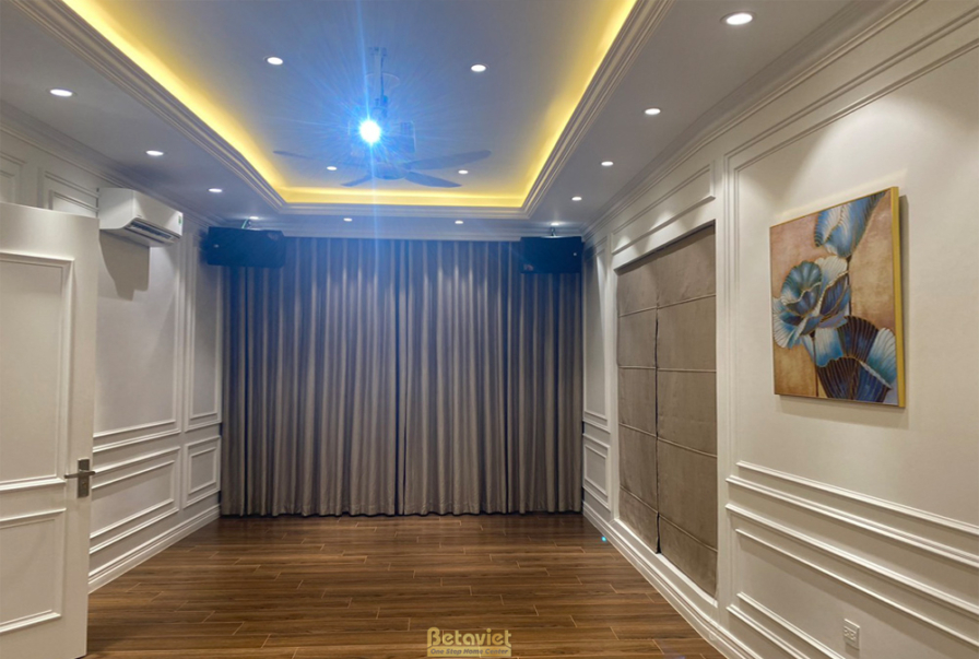 Phòng sinh hoạt chung hoặc phòng giải trí với sàn gỗ, tường ốp phào chỉ trắng. Trần thạch cao giật cấp với đèn hắt, rèm cử…
