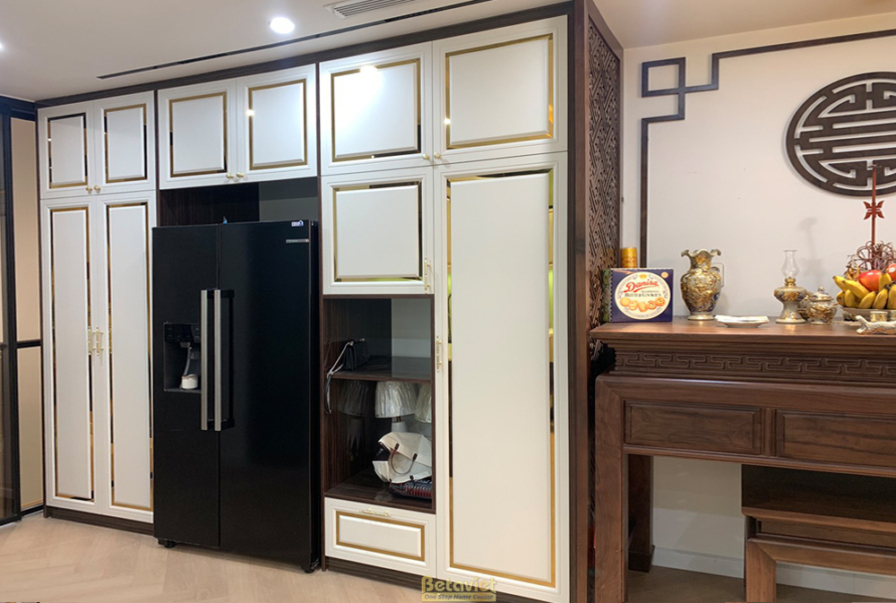 Tủ bếp và tủ lạnh âm tường màu trắng kem kết hợp đen, viền kim loại vàng. Thiết kế hiện đại, tối ưu không gian, mang lại s…