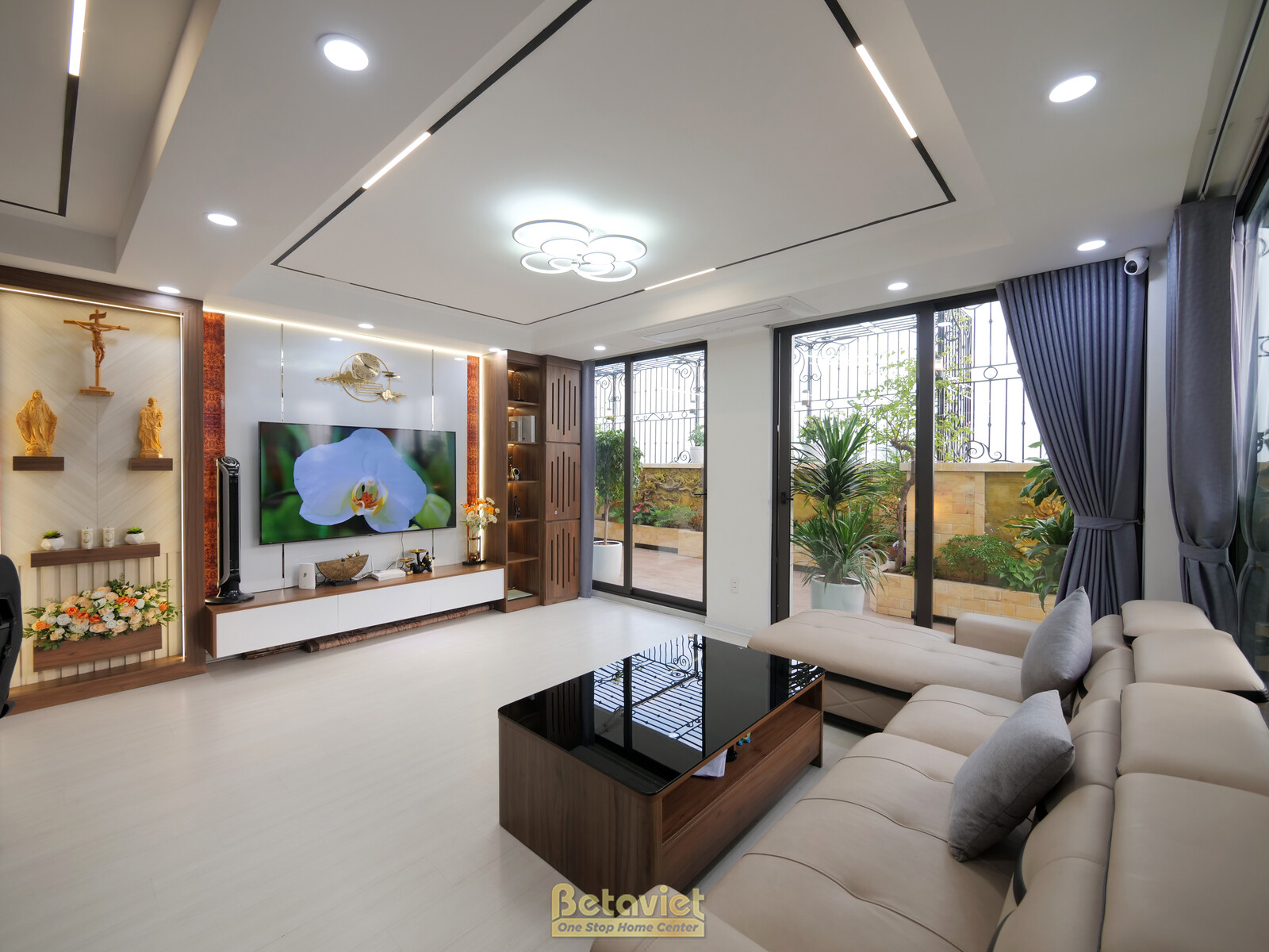 Phòng khách rộng rãi với sofa chữ L màu be, bàn trà mặt đá đen. Góc nhìn từ cửa, bao quát khu vực sinh hoạt chính và ban c…