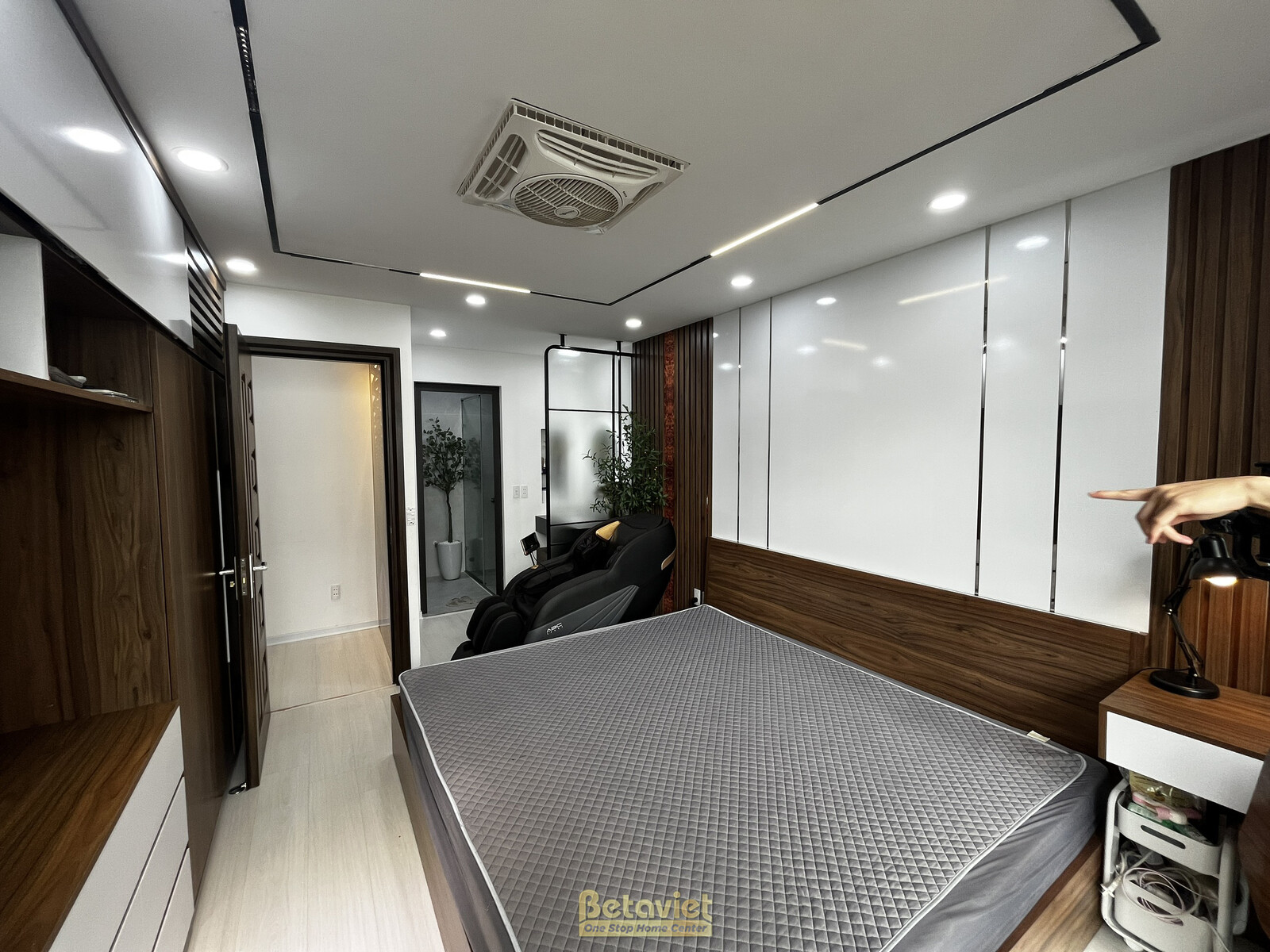 Phòng ngủ master hiện đại với giường lớn, đầu giường ốp gỗ và vách trang trí. Hệ tủ quần áo âm tường màu trắng và nâu gỗ c…