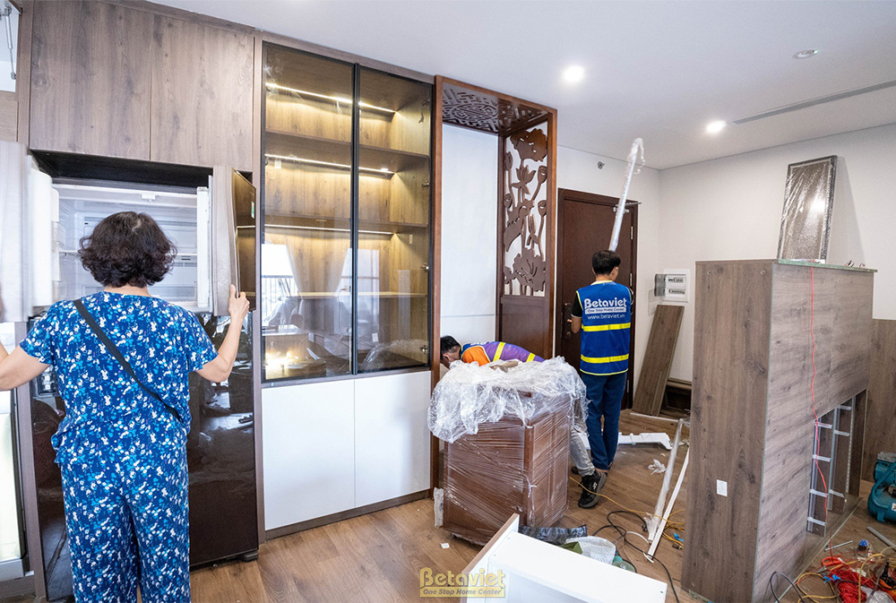 Khu vực bếp hoặc phòng ăn với hệ tủ trưng bày lớn bằng gỗ và kính, đang trong quá trình lắp đặt. Các chi tiết được chăm ch…