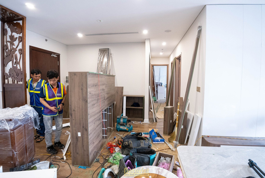 Cảnh thi công lắp đặt hệ tủ gỗ tại khu vực hành lang hoặc sảnh vào. Các thợ đang cẩn thận ghép nối các module tủ, chuẩn bị…