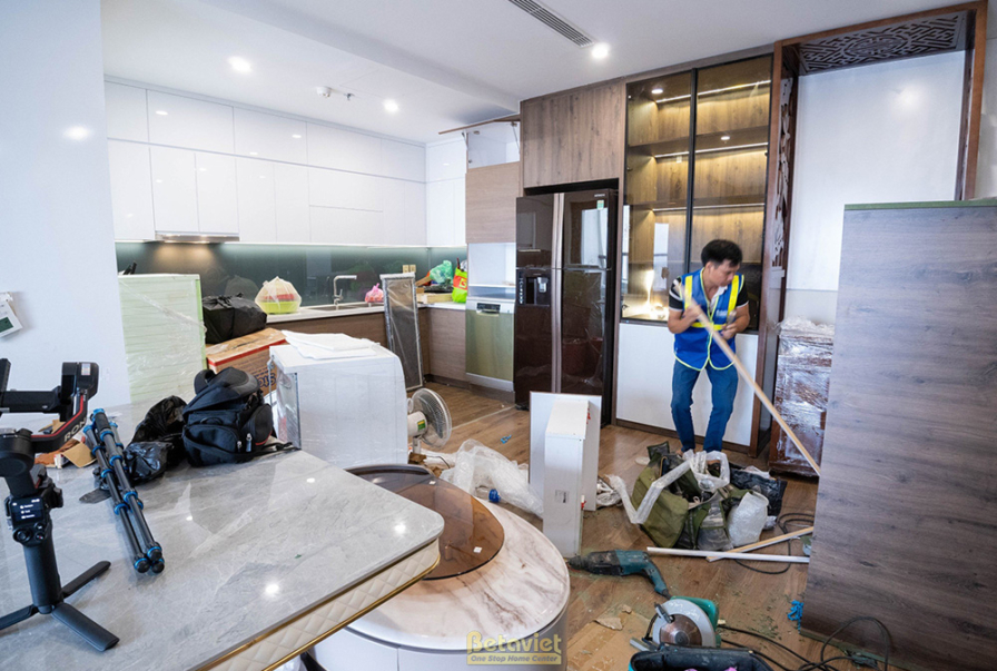 Cảnh thi công lắp đặt khu vực bếp, tủ bếp trên dưới màu trắng với mặt đá và ốp tường kính màu xanh ngọc. Một thợ đang kiểm…