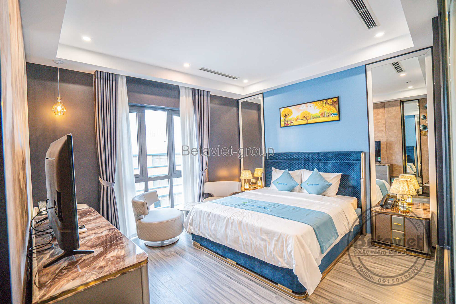 Góc nhìn khác của phòng ngủ khách sạn, tập trung vào giường ngủ và khu vực bàn trang điểm. Tường màu xanh nhạt, gương lớn…