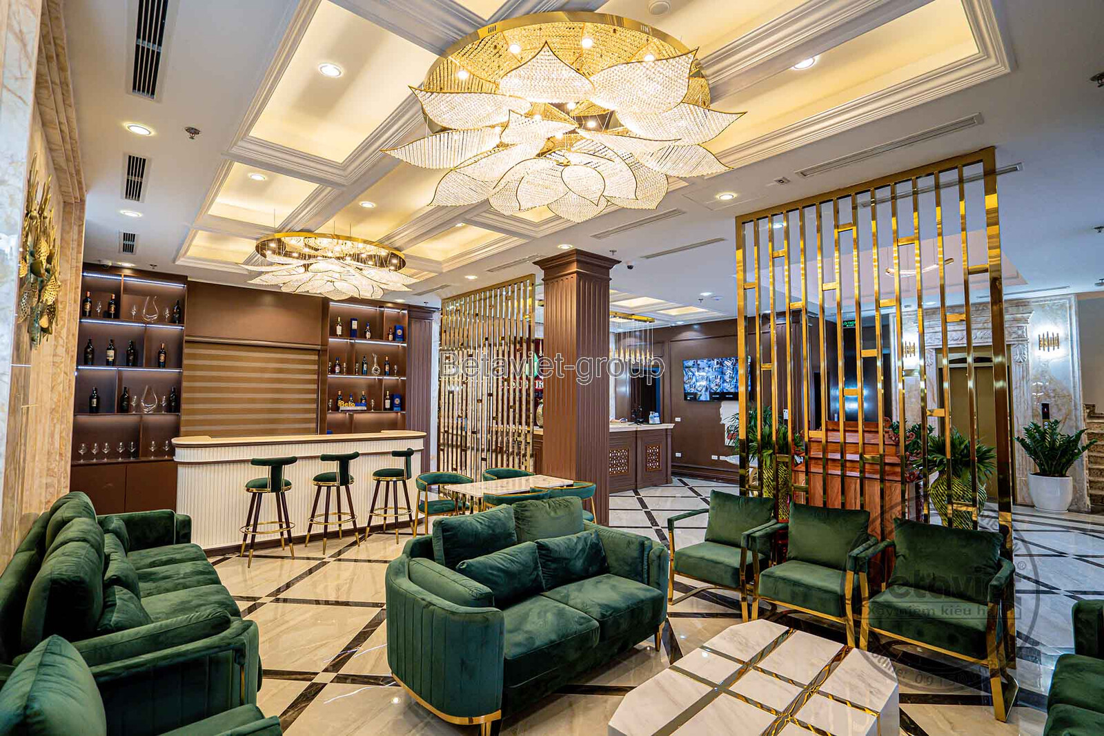 Không gian sảnh chờ khách sạn sang trọng với bộ sofa bọc nhung xanh đậm, bàn trà mặt đá và khung kim loại ánh vàng. Hệ đèn…