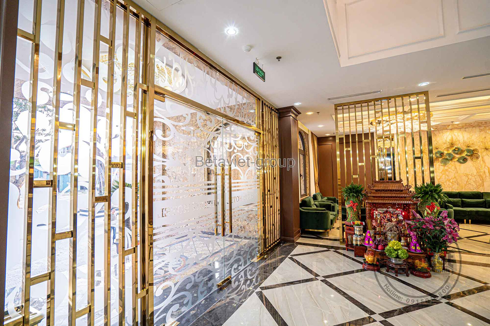 Sảnh hành lang khách sạn với sàn đá hoa văn đối xứng, vách ngăn kim loại mạ vàng và gương lớn tạo cảm giác rộng rãi. Ghế s…