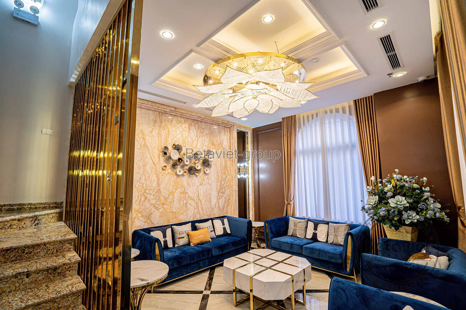 Không gian phòng khách sang trọng với bộ sofa bọc nhung màu xanh coban nổi bật. Tường ốp đá vân tự nhiên kết hợp decor ngh…