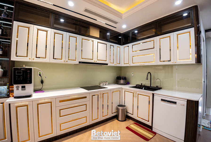 Góc bếp với hệ tủ trên dưới màu trắng kem viền vàng, mặt bếp đá trắng. Thiết bị bếp hiện đại, không gian sáng sủa, tối ưu…