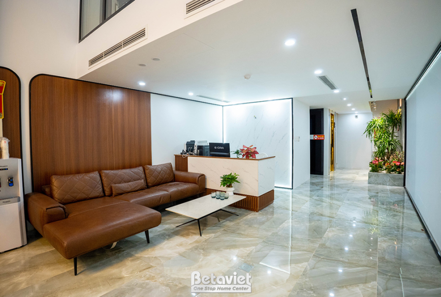Phòng khách rộng rãi với sofa da màu nâu, bàn trà gỗ. Tường ốp gỗ và đá, sàn đá bóng. Ánh sáng tự nhiên và đèn trần, tạo k…