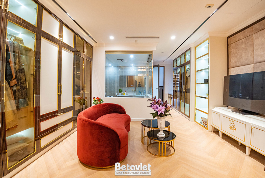 Phòng khách sang trọng với sofa nhung đỏ đô, bàn trà tròn. Tường ốp gỗ và phào chỉ trắng, sàn gỗ xương cá. Ánh sáng ấm áp…