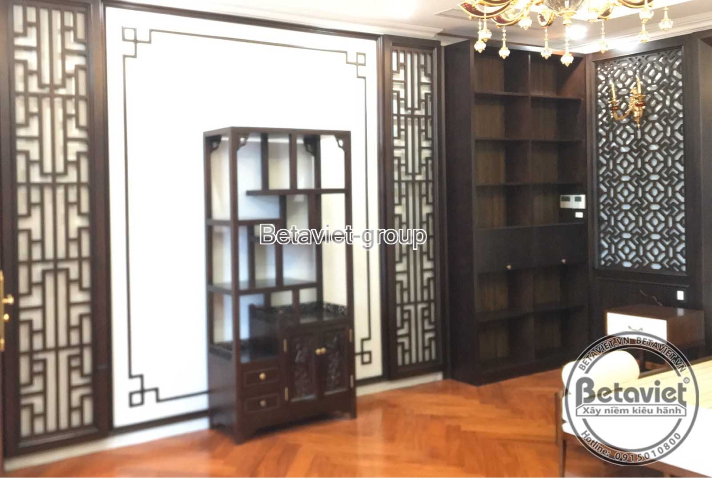 Không gian phòng ngủ đang lắp đặt nội thất gỗ tối màu, bao gồm vách đầu giường và tủ kệ trang trí, mang phong cách Á Đông…