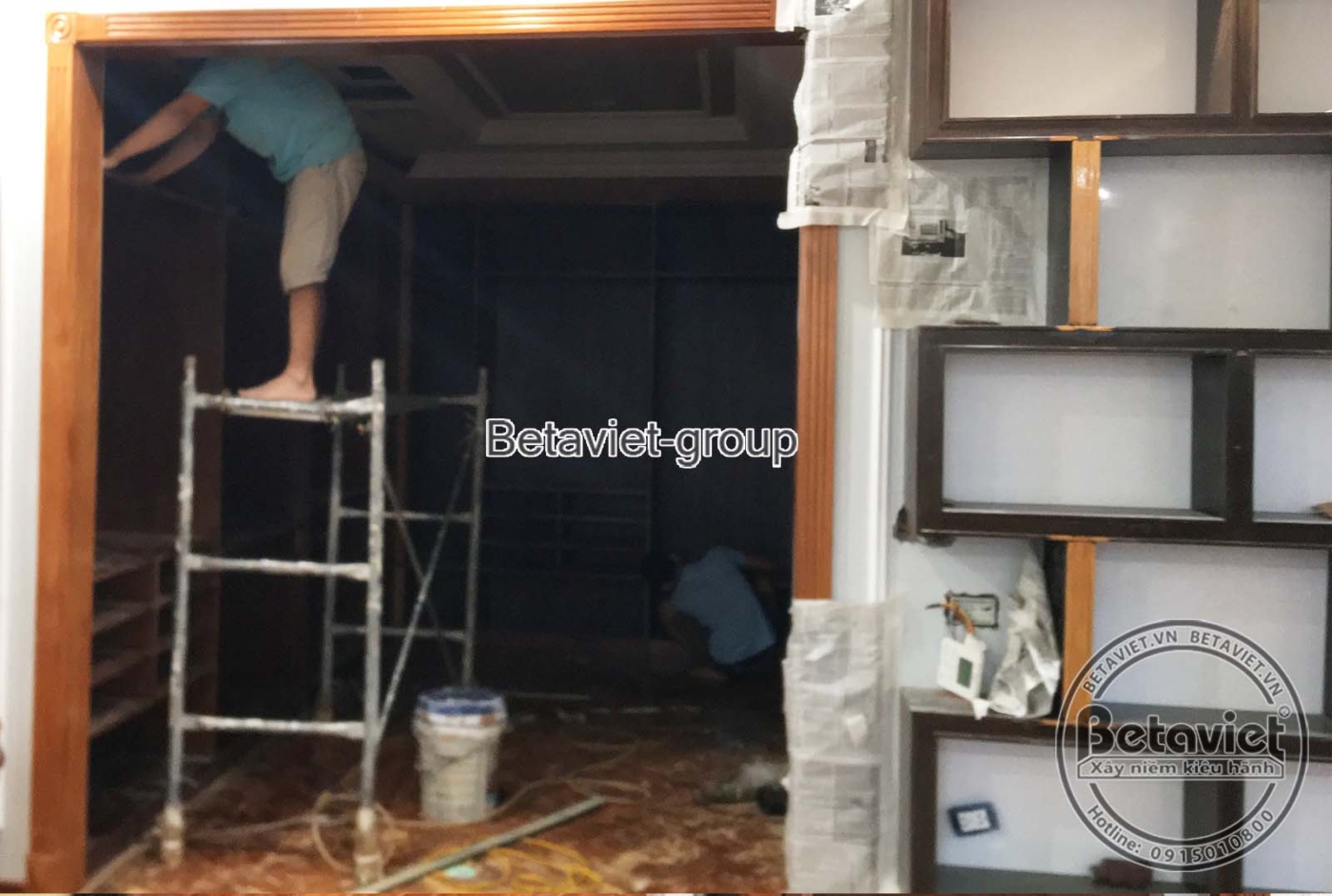 Không gian phòng ngủ đang lắp đặt nội thất gỗ tối màu, với vách đầu giường màu trắng và các chi tiết trang trí tinh tế, tạ…