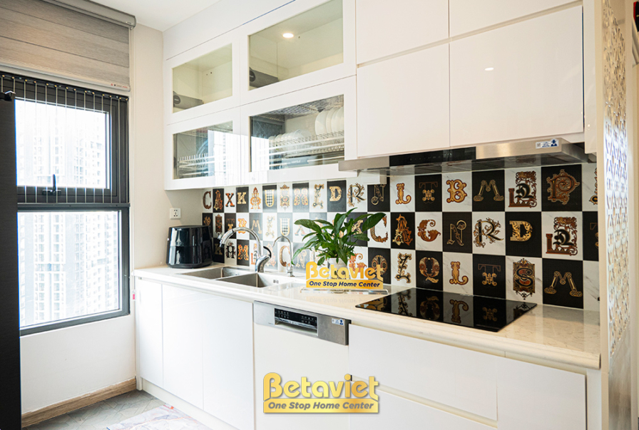 Cận cảnh khu vực bếp với tủ bếp trên và dưới màu trắng acrylic sáng bóng, mặt đá quartz trắng sang trọng. Bếp từ âm và hút…