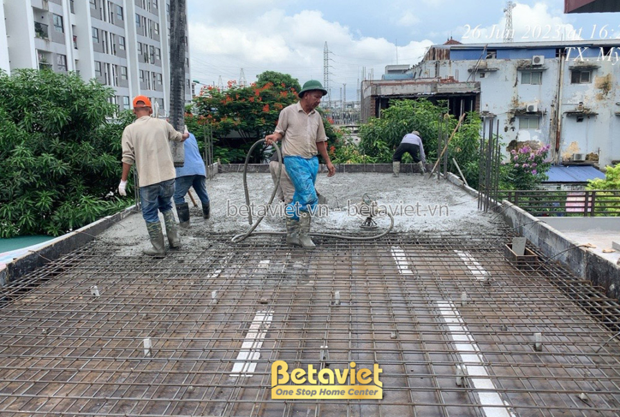 Công nhân đang san phẳng bê tông trên sàn tầng, đảm bảo bề mặt phẳng và đúng kỹ thuật. Khung sắt thép đã được phủ một phần…