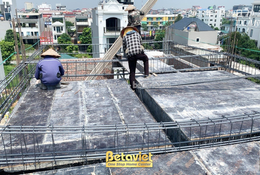 Công nhân đang thi công trên sàn bê tông tầng trên cùng, kiểm tra và chuẩn bị cho việc đổ bê tông. Khung sắt thép được bố…