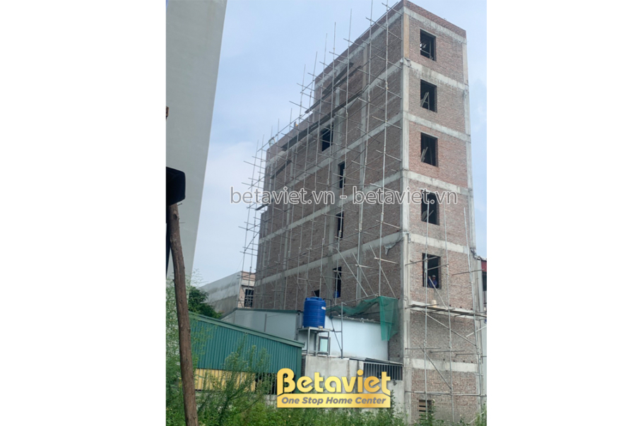 Mặt tiền công trình nhà phố 6 tầng đang trong giai đoạn xây thô, có giàn giáo bao quanh. Các ô cửa sổ đã định hình, tường…