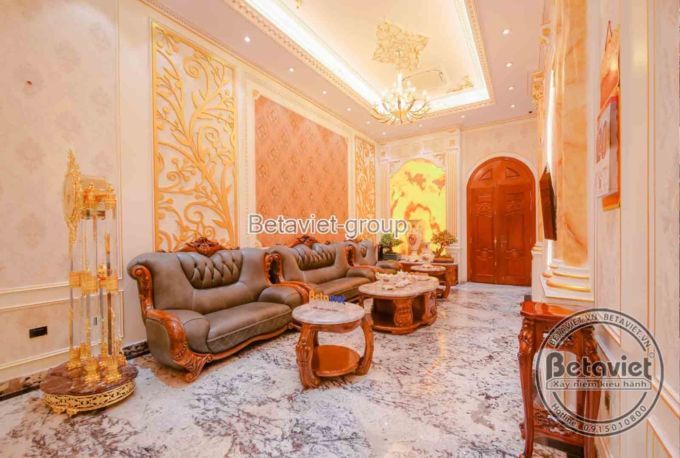 Phòng khách sang trọng với bộ sofa bọc da màu nâu, bàn trà gỗ chạm khắc tinh xảo, đặt trên sàn đá vân mây. Tường ốp hoa vă…