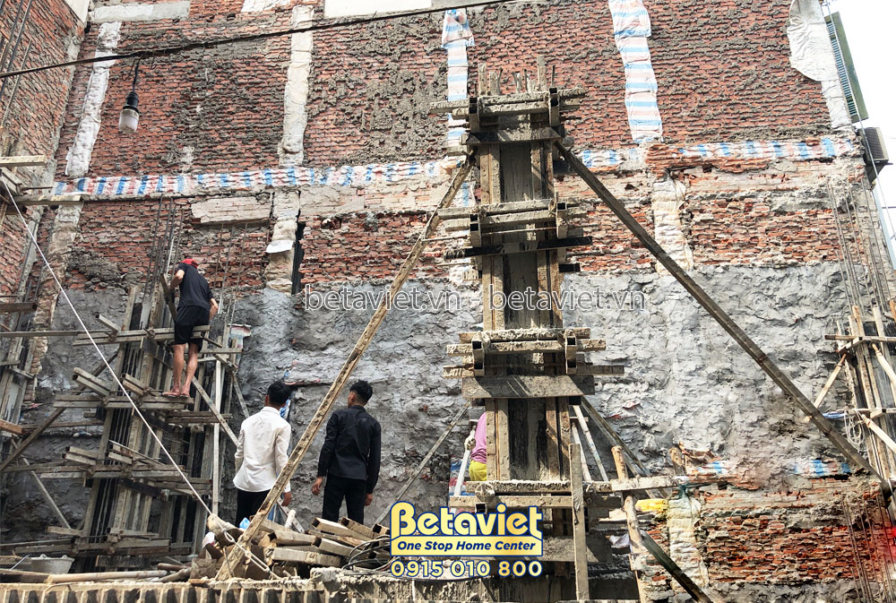 Góc thi công cột bê tông sát tường gạch cũ, ván khuôn gỗ chống cột dựng chắc chắn theo phương thẳng đứng. Gạch đỏ, gỗ cốp…
