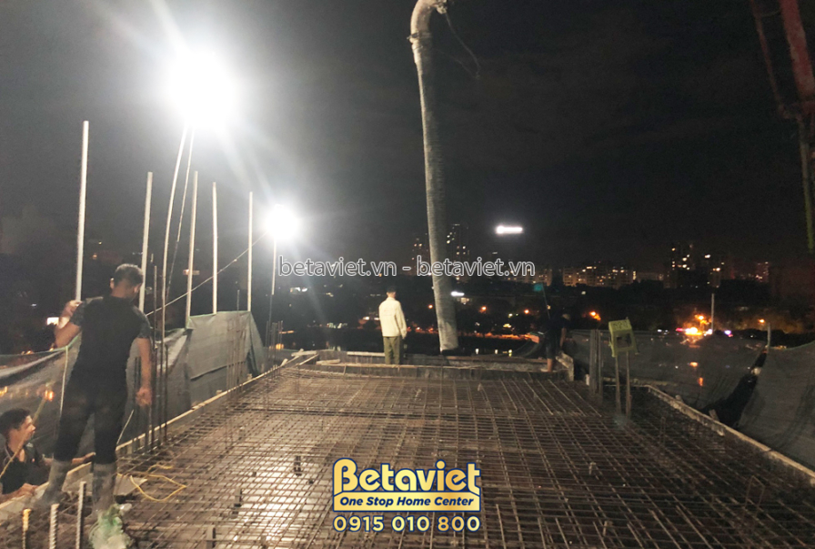 Công nhân đang đổ bê tông sàn vào ban đêm, với hệ thống cốt thép đã được chuẩn bị sẵn. Ánh sáng từ đèn chiếu sáng công trư…