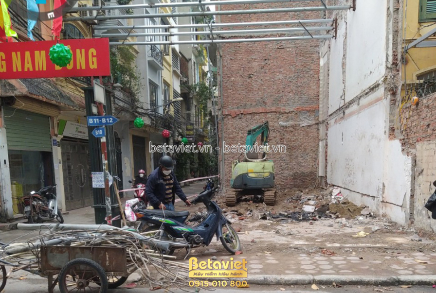 Toàn cảnh công trường nhà phố từ góc nhìn đường phố, máy xúc đang làm việc trên nền đất. Xung quanh là các nhà dân và biển…