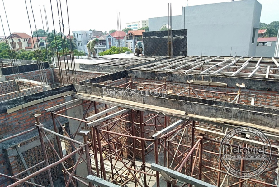 Khung sàn bê tông cốt thép tầng cao với ván khuôn gỗ đỡ dầm, cột thép chờ nhô lên chuẩn bị đổ tầng tiếp theo. Xung quanh l…
