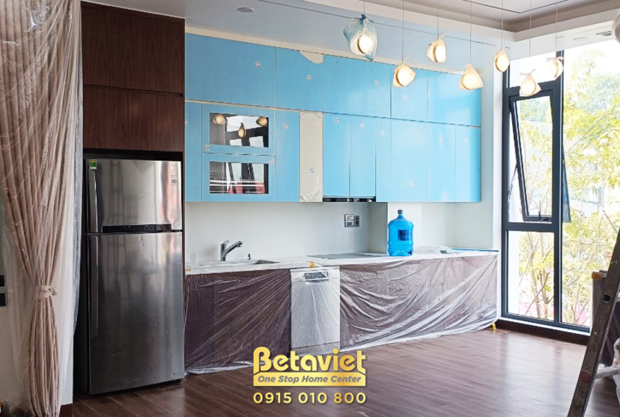 Không gian bếp hiện đại với tủ bếp trên màu xanh pastel và tủ bếp dưới màu gỗ. Bàn đảo bếp màu trắng, thiết bị nhà bếp bằn…