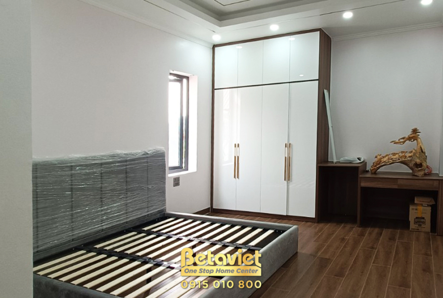 Phòng ngủ với giường bọc nệm màu xám, tủ quần áo lớn màu trắng và tủ đầu giường gỗ. Không gian rộng rãi, ánh sáng tự nhiên…