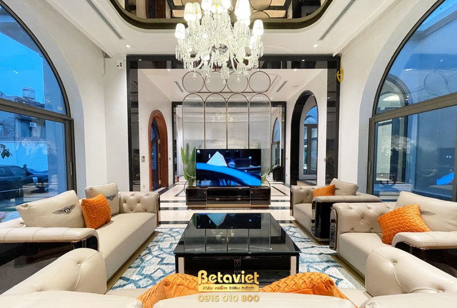 Phòng khách duplex nhìn thẳng từ khu vực cầu thang, tập trung vào trung tâm không gian. Bộ sofa da màu kem bố trí đối xứng…