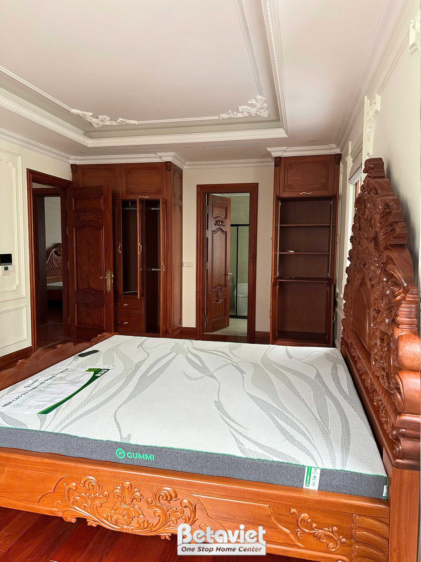 Phòng ngủ hoàn thiện với giường gỗ tự nhiên chạm khắc đầu giường cầu kỳ, đệm trắng mới lắp còn nguyên tem. Tủ gỗ và cửa ph…