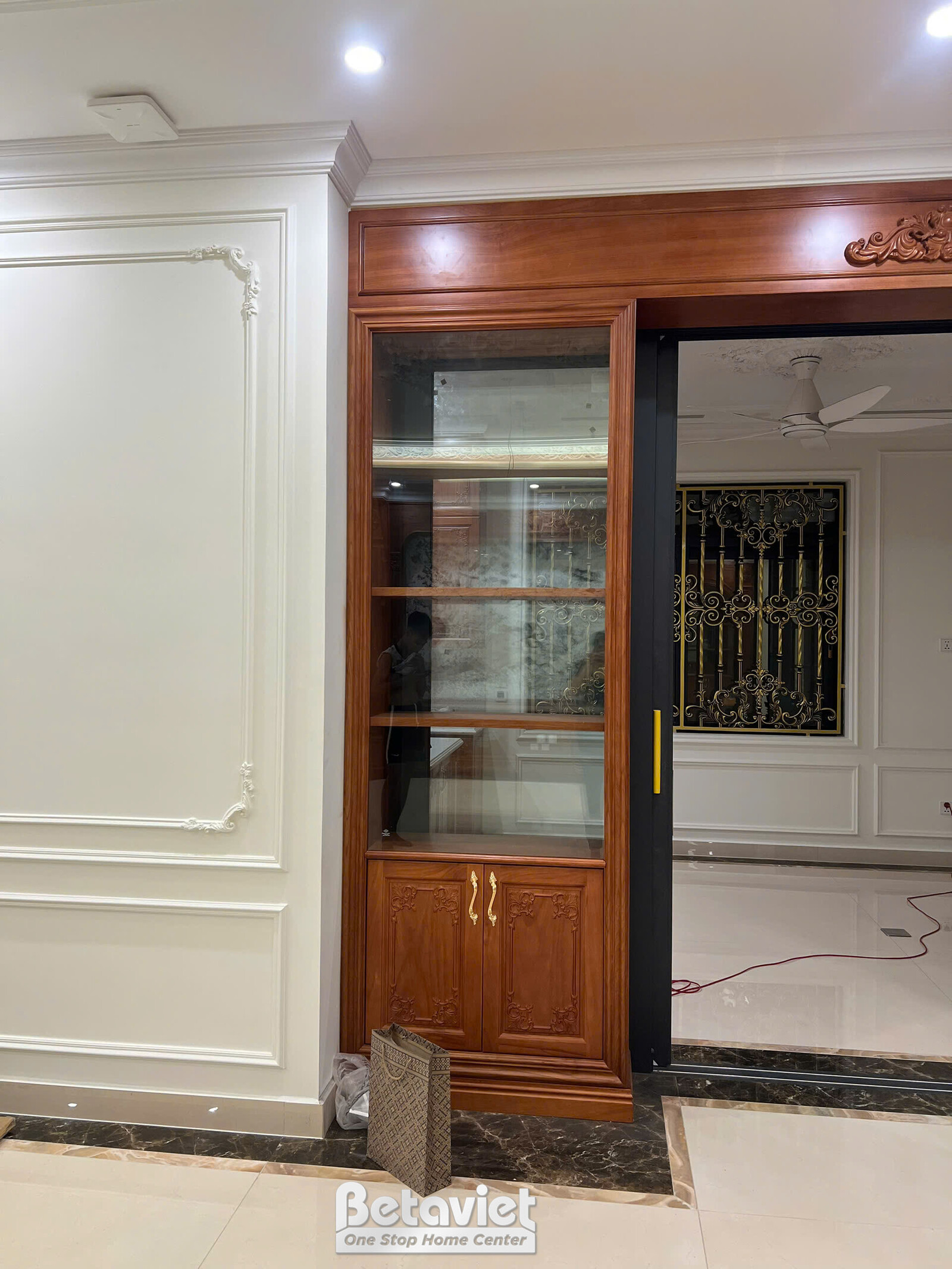 Góc tủ kệ trang trí gỗ tự nhiên kết hợp cửa kính, đặt trong hốc tường ốp phào chỉ trắng tinh tế. Đèn LED hắt sáng từ trên…