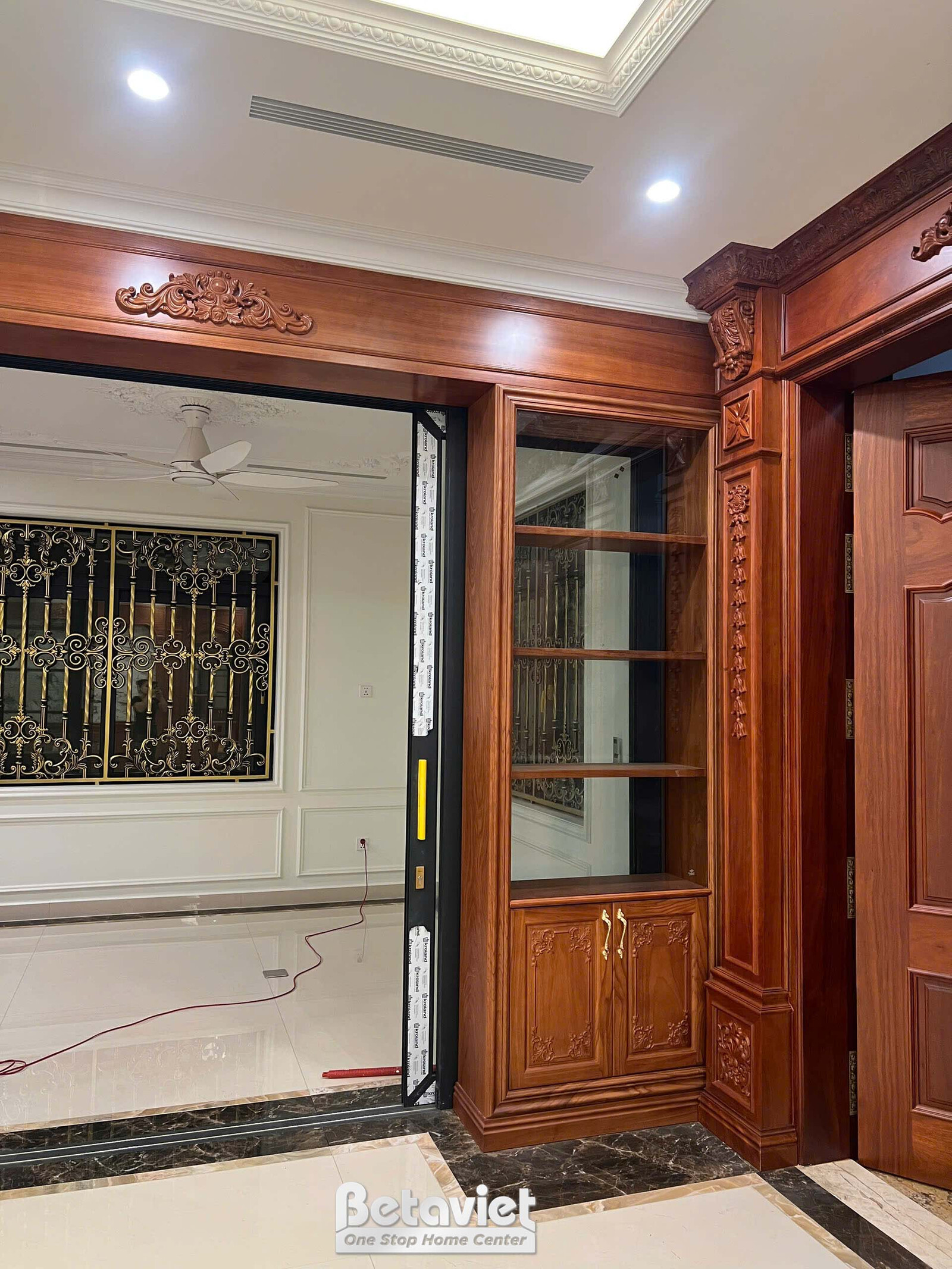 Cửa trượt lớn bằng gỗ tự nhiên và kính, màu nâu đỏ, ngăn cách các không gian. Tường ốp phào chỉ trắng, sàn đá sáng màu, tạ…