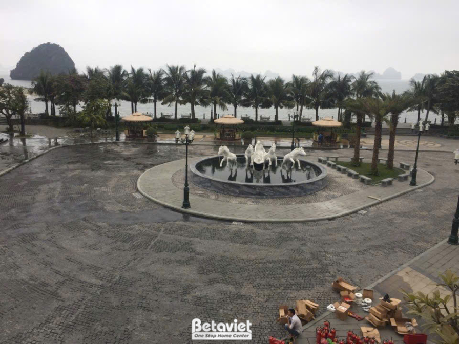 Cận cảnh đài phun nước hình tượng ngựa tại quảng trường trung tâm, với dòng nước chảy mềm mại. Phía sau là khung cảnh biển…