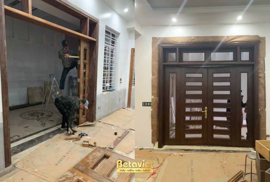 Khu vực sảnh hoặc phòng khách đang lắp đặt hệ cửa gỗ lớn và vách ốp tường bằng gỗ màu nâu trầm. Sàn nhà được bảo vệ bằng v…