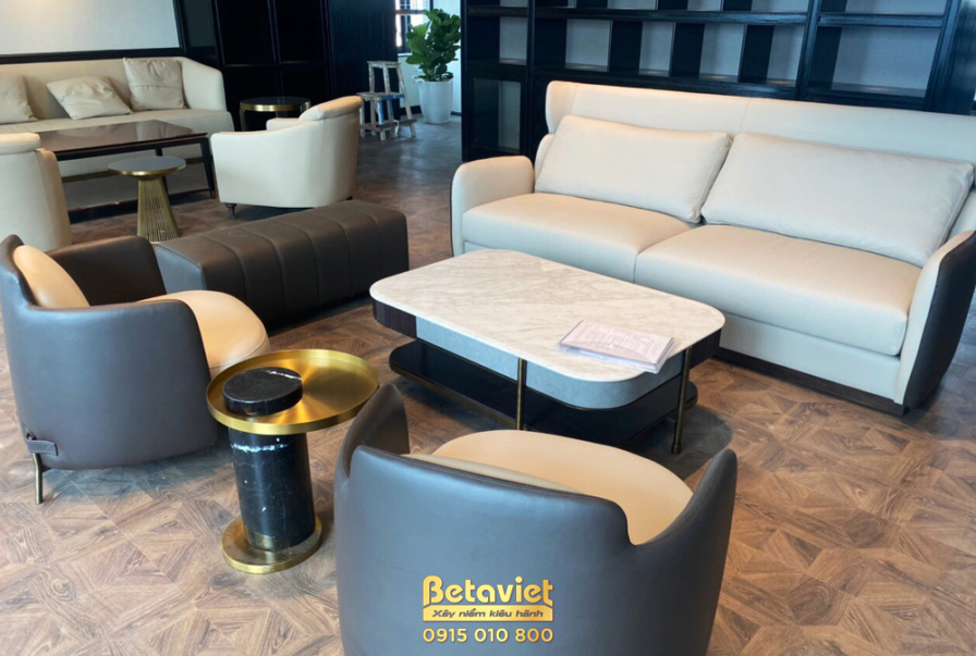 Khu vực phòng khách phụ hoặc tiếp khách riêng tư với sofa dài màu kem, hai ghế đơn bọc da màu xám và bàn trà mặt đá trắng…