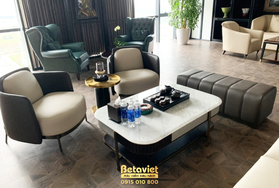Khu vực tiếp khách nhỏ với hai ghế sofa đơn bọc da màu be và xám, bàn trà mặt đá trắng hình oval. Bố cục đối xứng, vật liệ…
