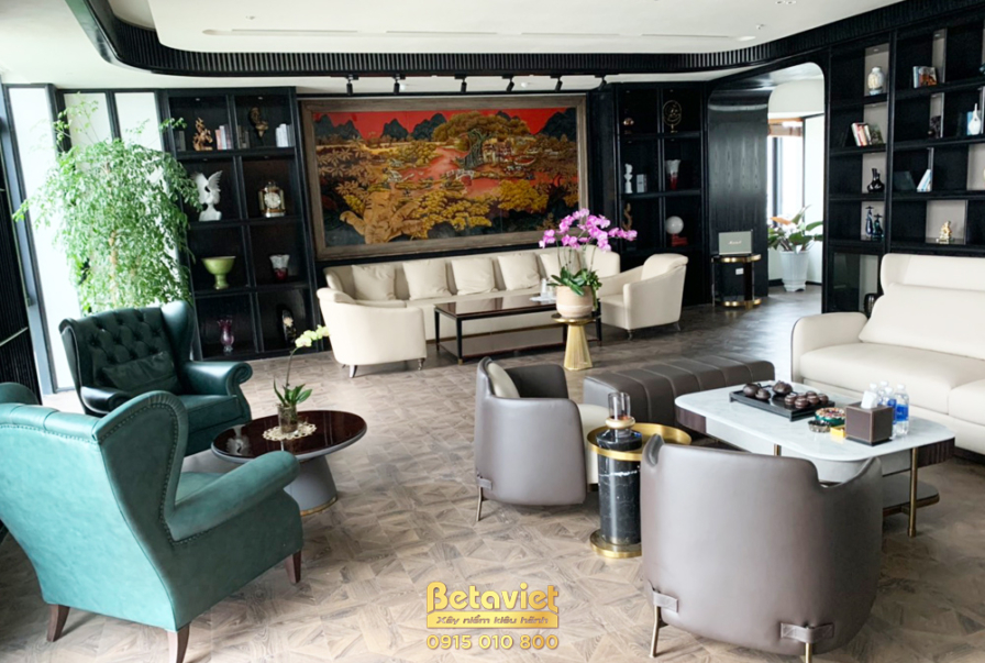 Góc phòng khách với sofa chữ L màu kem, bàn trà mặt đá trắng. Điểm nhấn là bức tranh lớn treo tường và hệ tủ kệ âm tường m…