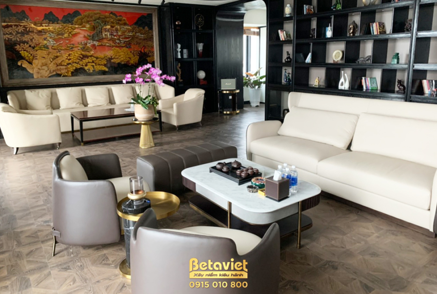 Không gian phòng khách rộng rãi với sofa chữ L màu kem, bàn trà mặt đá trắng. Bố cục mở, kết nối với khu vực khác. Ánh sán…