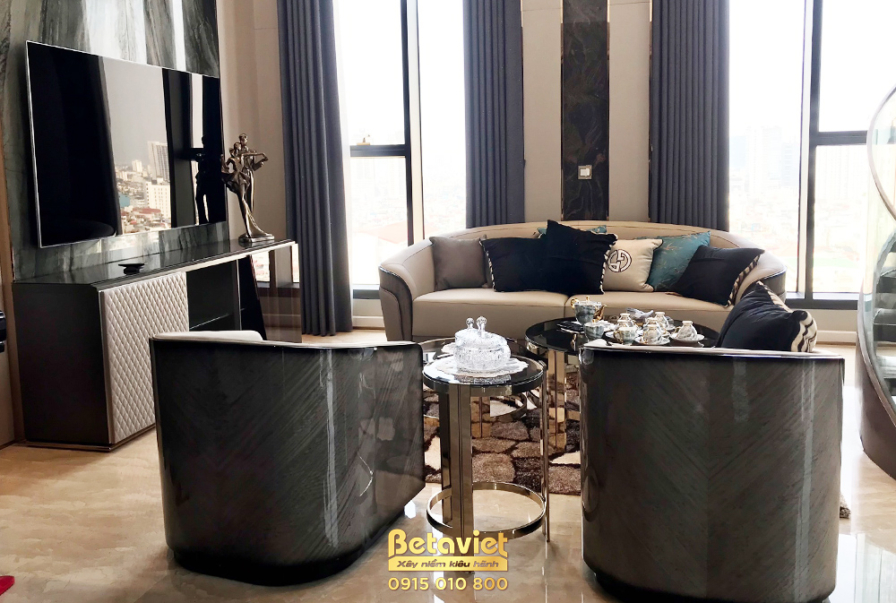 Toàn cảnh phòng khách penthouse với bố cục mở, nơi bộ sofa và ghế đơn màu be được sắp đặt hài hòa với kệ TV hiện đại. Các…