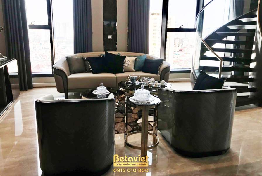 Không gian phòng khách penthouse nhìn từ góc rộng, nổi bật với bộ sofa và hai ghế đơn bọc da màu be sang trọng, đặt đối di…